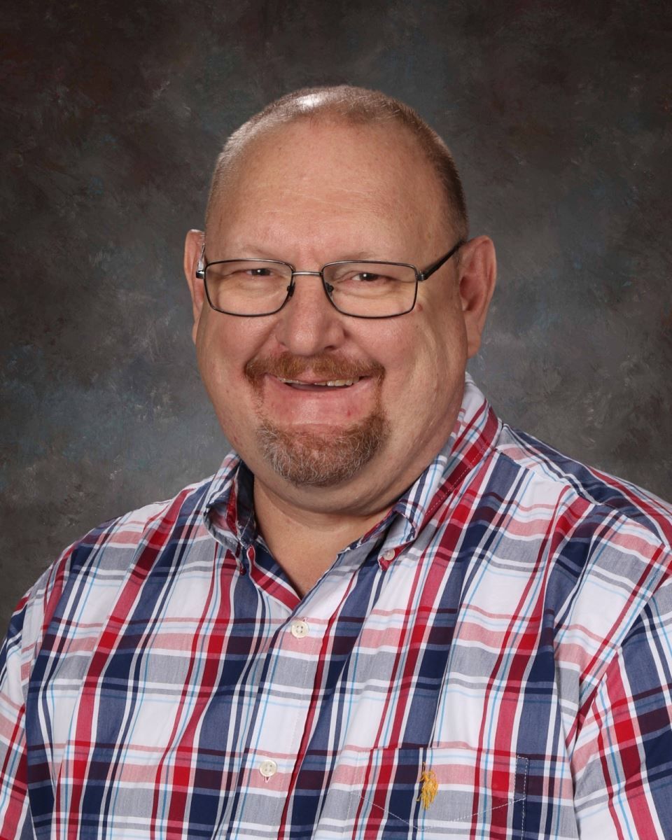 A man wearing glasses and a plaid shirt is smiling for the camera.