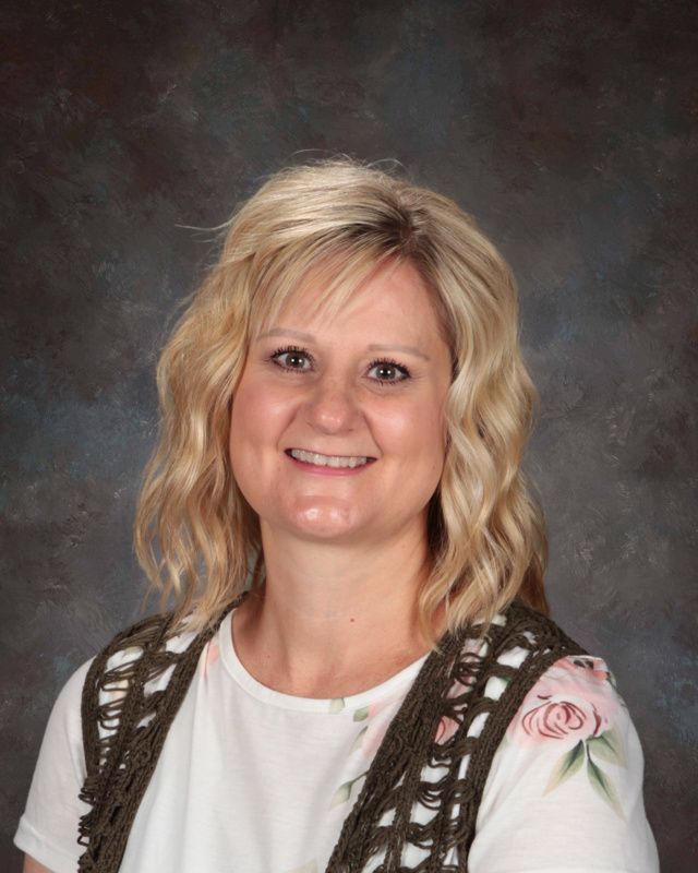 A woman wearing a white shirt and a brown vest is smiling for the camera.