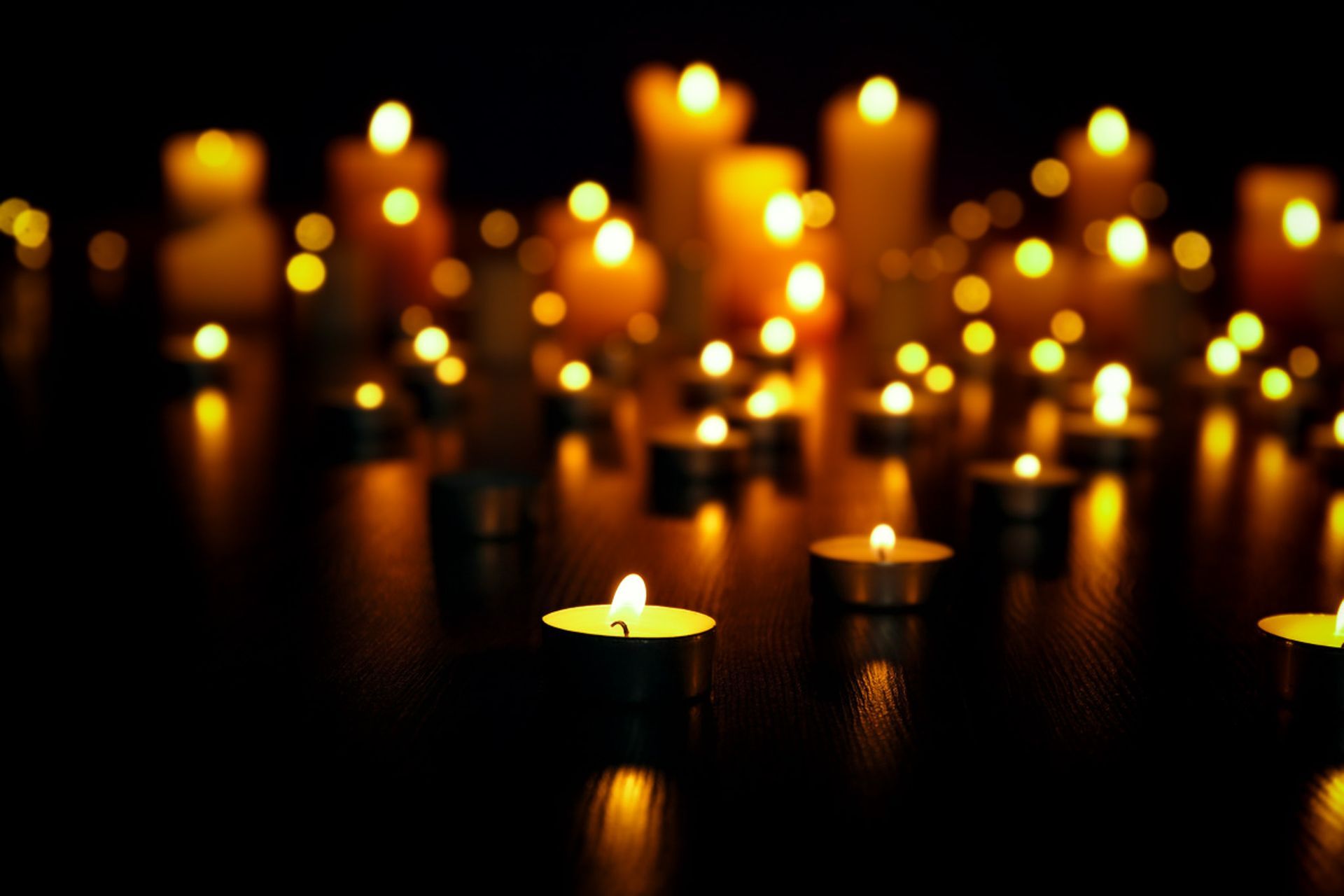Glowing candles in a dark, blurred background with warm yellow lights reflected on a surface