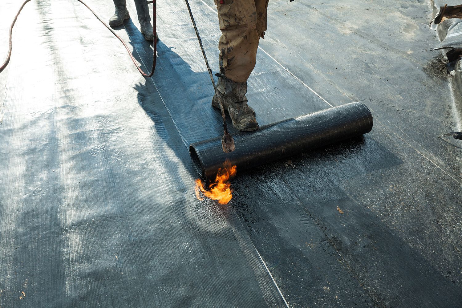 Worker torching roofing material on a flat roof, with flames at the seam. Worker torching roofing material on a flat roof, with flames at the seam.