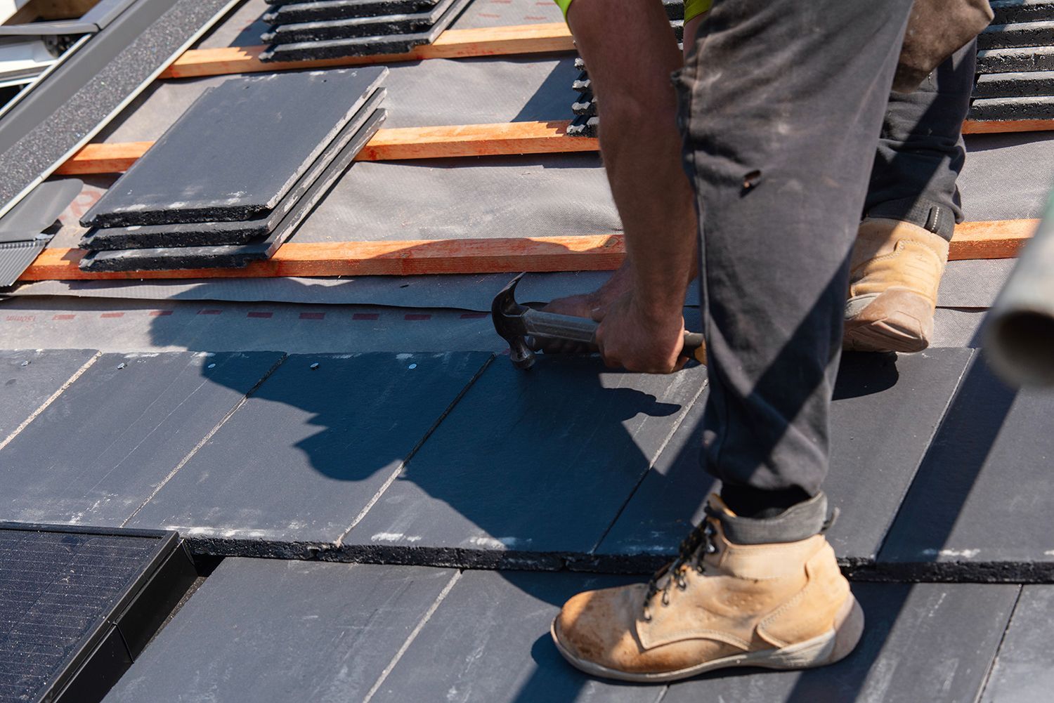 Worker installing dark roof panels on a sloped roof with orange battens