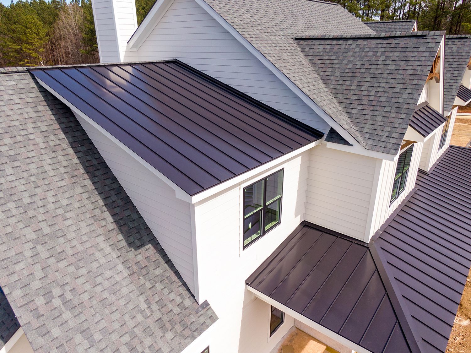 Aerial view of a house roof with gray shingles and a dark metal standing-seam section. Aerial view of a house roof with gray shingles and a dark metal standing-seam section.
