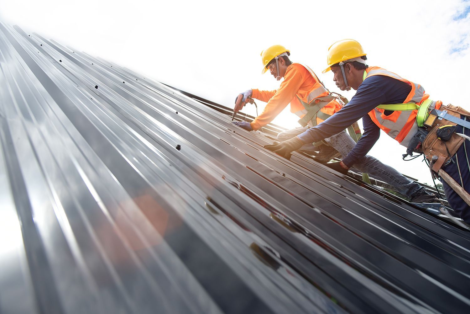 Workers in hard hats installing metal roofing on a steep roof with sunlight glare Workers in hard hats installing metal roofing on a steep roof with sunlight glare