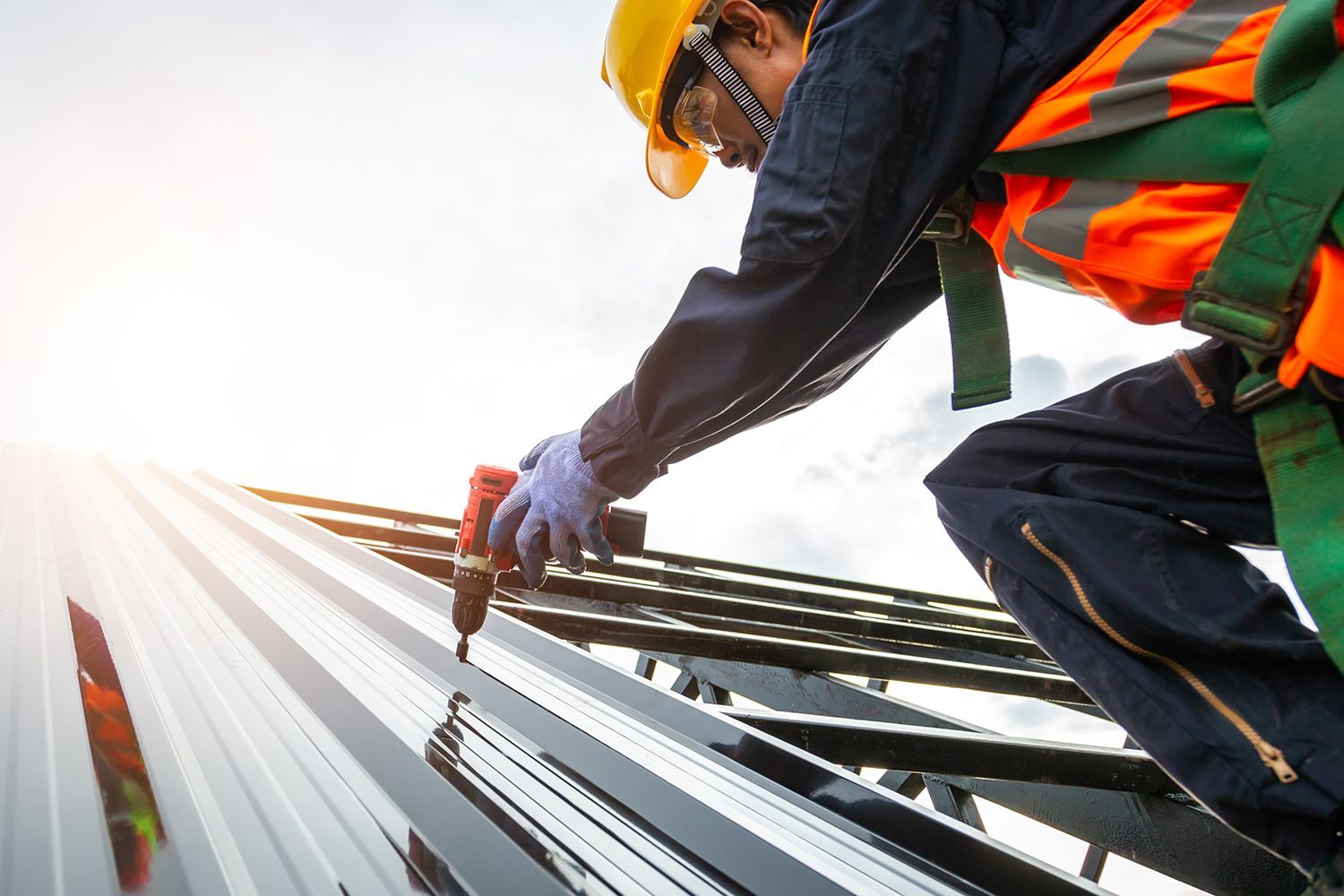 Worker in hard hat and safety vest inspecting metal roofing in bright sunlight Worker in hard hat and safety vest inspecting metal roofing in bright sunlight