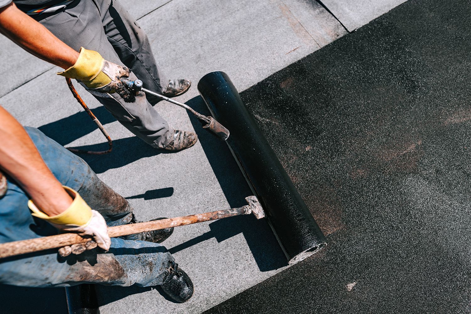 Workers using rollers to apply black roofing material on a flat roof Workers using rollers to apply black roofing material on a flat roof