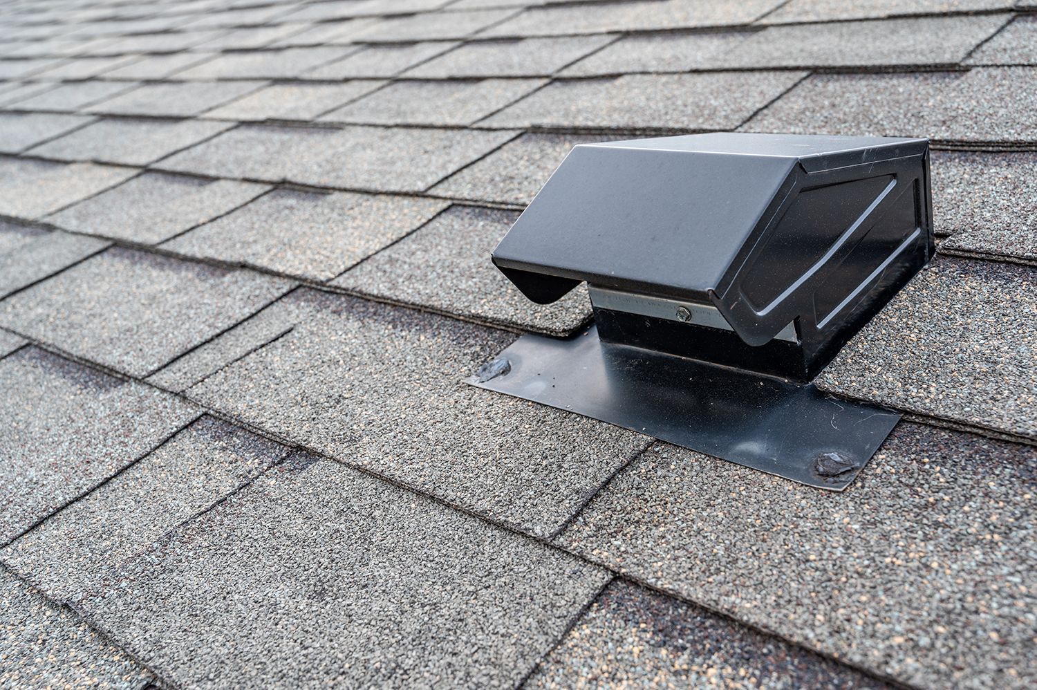 Black roof vent on gray shingled roof with metal flashing Black roof vent on gray shingled roof with metal flashing