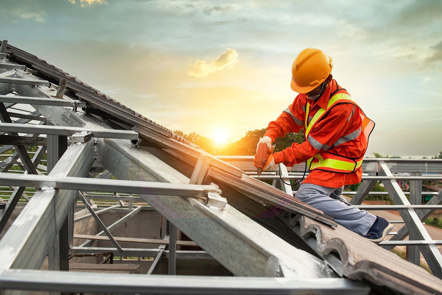 Construction worker in orange safety gear securing metal beams on a rooftop at sunrise Construction worker in orange safety gear securing metal beams on a rooftop at sunrise