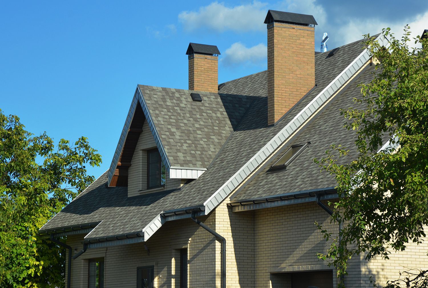 Brick house with two chimneys and a steep gray shingled roof under a blue sky Brick house with two chimneys and a steep gray shingled roof under a blue sky