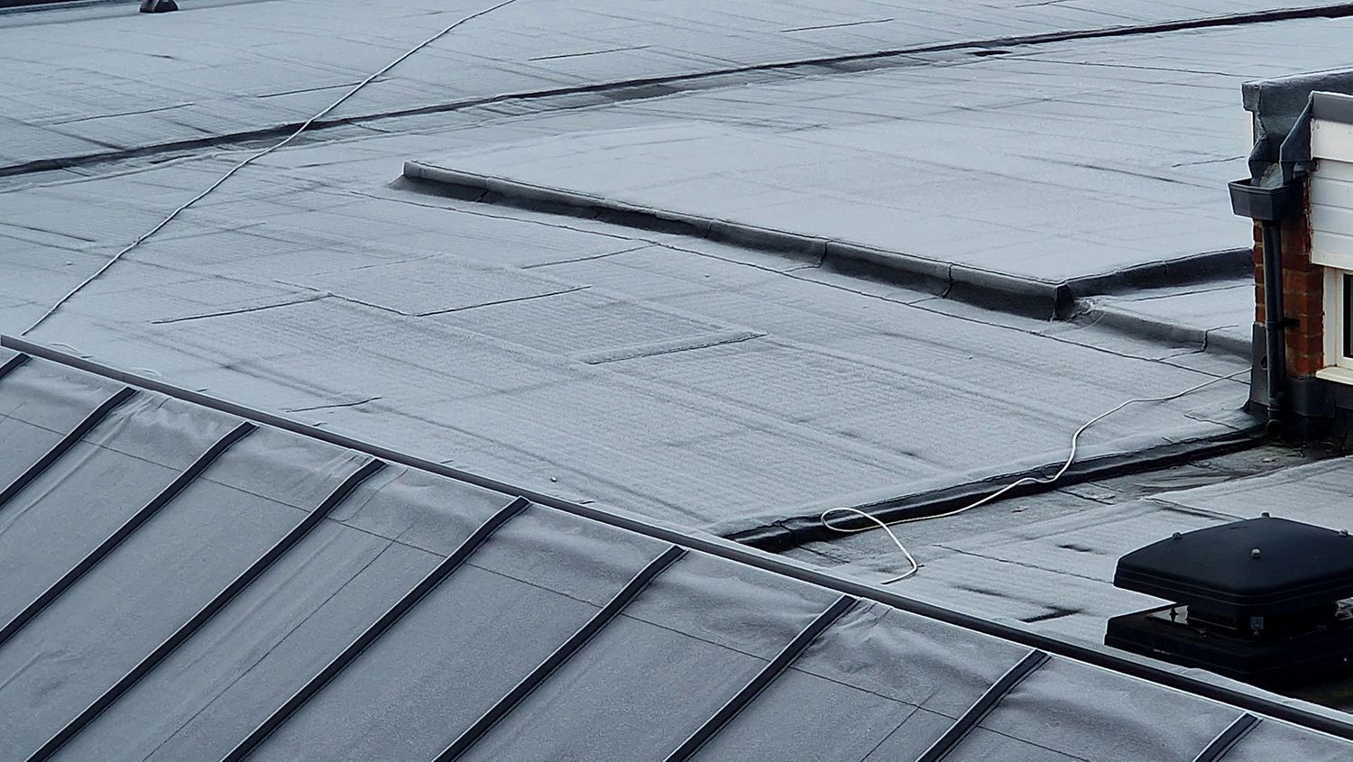 Rainwater on a gray metal roof with seams and a small roof vent. Rainwater on a gray metal roof with seams and a small roof vent.