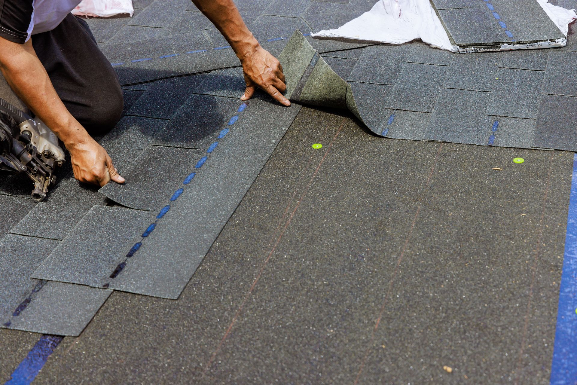 Worker installing gray roof shingles with blue chalk lines on a rooftop
