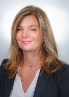 Portrait of a smiling woman with light brown hair in a dark blazer and white blouse