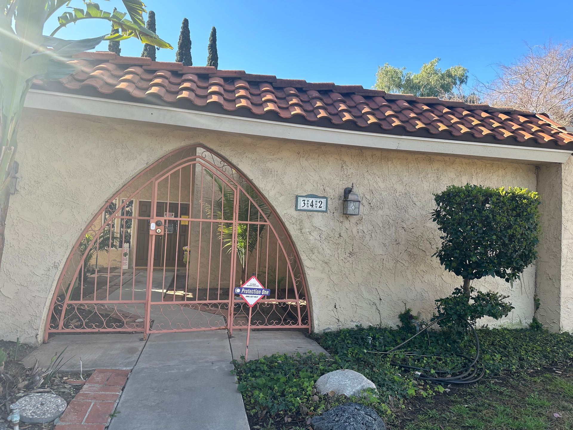 Tan stucco home with a terracotta tile roof and pink arched gate; address number 