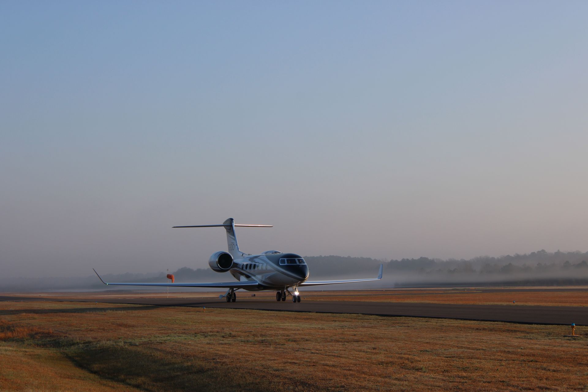 A private jet taxis on an airport runway during a hazy, golden-hour sunrise.