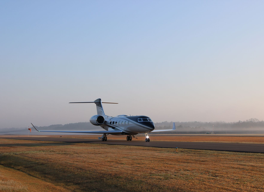 Small private jet taxiing on a runway at dawn, with a hazy sky and grassy foreground.