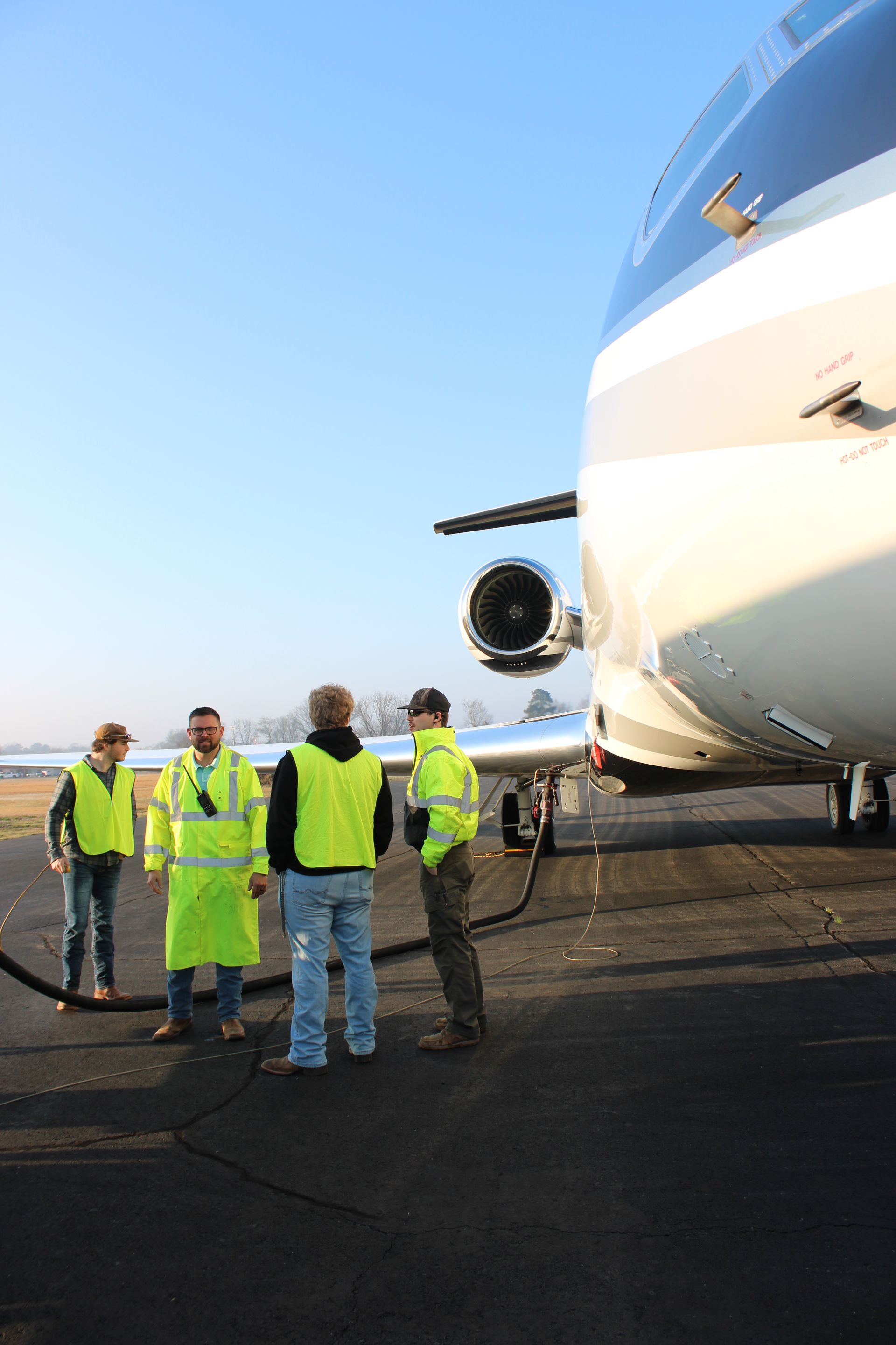 Four ground crew members in bright yellow safety vests stand on an airport tarmac next to a private jet.