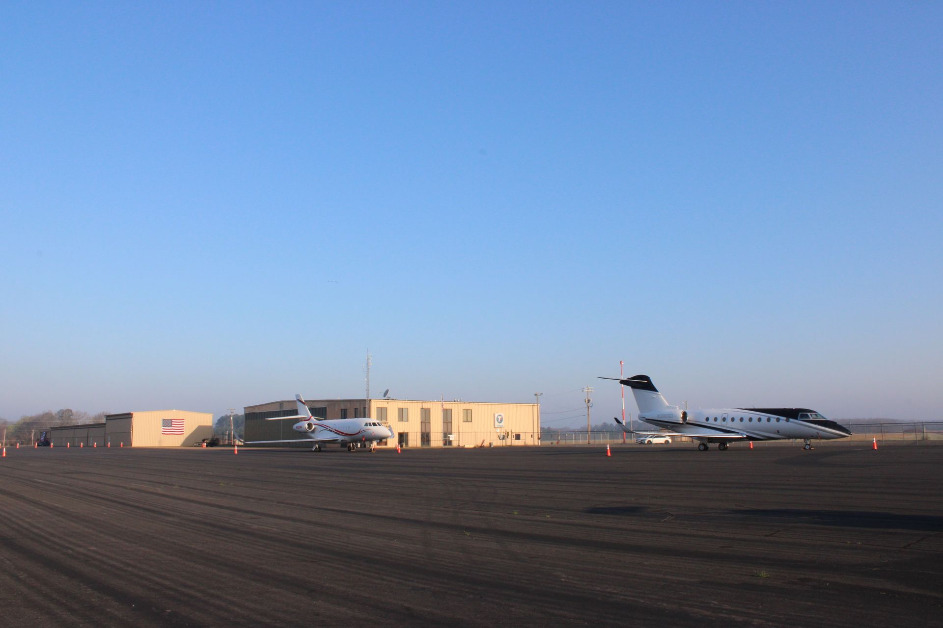 Two corporate jets parked on a tarmac in front of a beige hangar building under a clear blue sky.