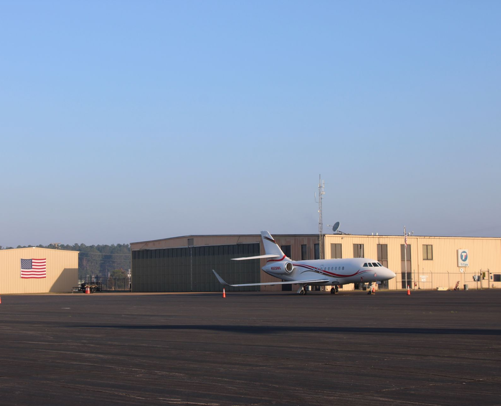 A private jet parked on an airport tarmac in front of a hangar with a prominent American flag.