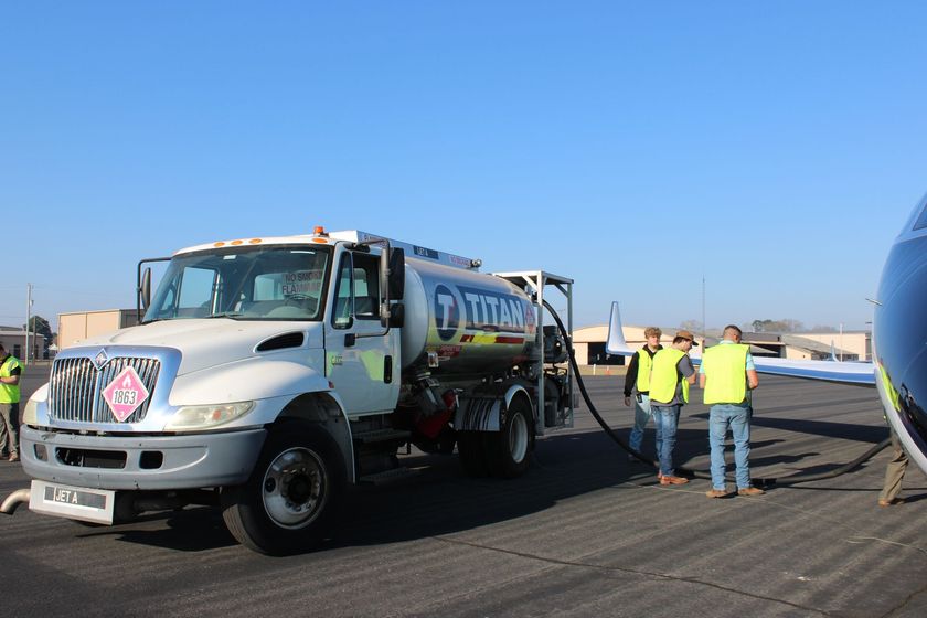 Fuel tanker truck on a road, with workers in safety vests standing beside it under a clear blue sky.