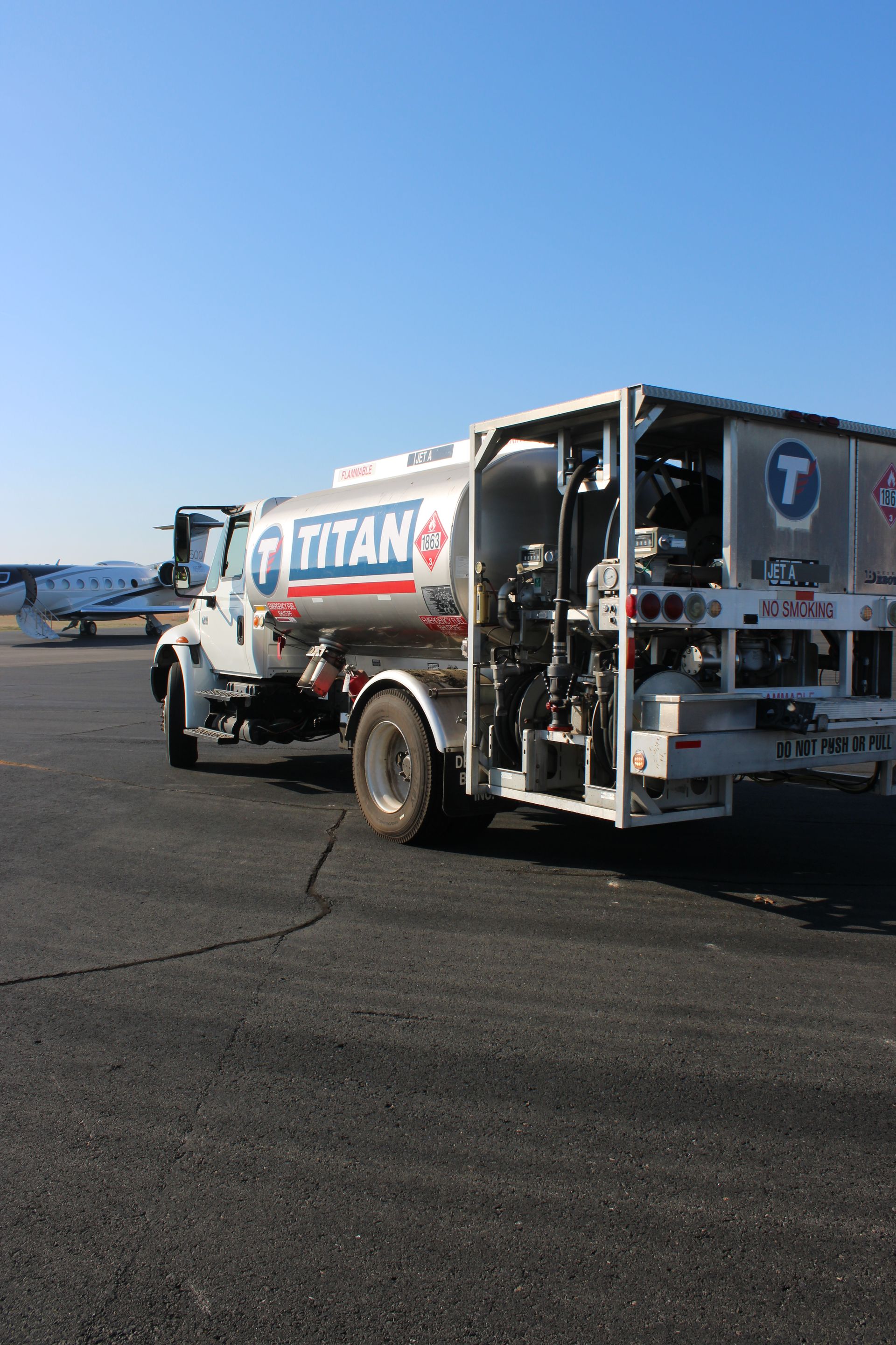 A Titan aviation fuel truck parked on an airport tarmac with a small aircraft in the background.