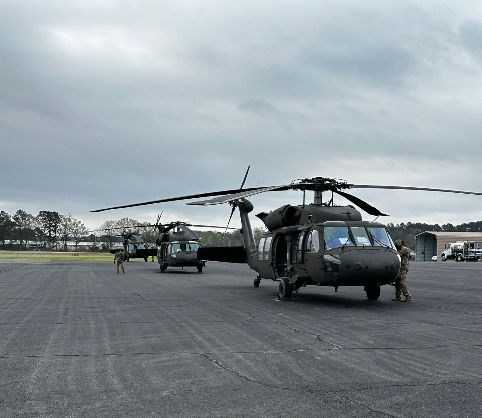 Two military helicopters parked on a runway under a cloudy sky