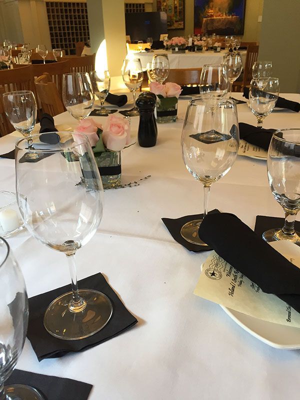 Set dining table with wine glasses, black napkins, and floral centerpieces at a formal event