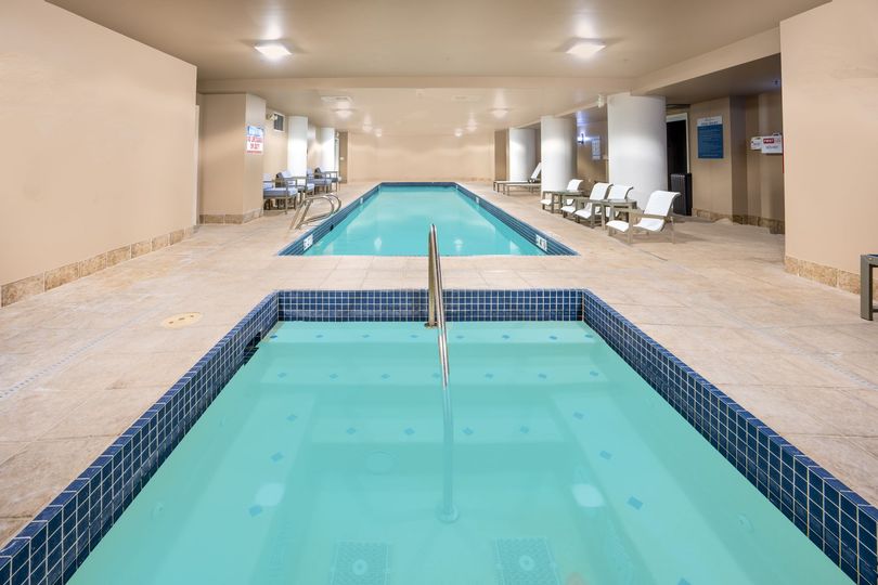 Indoor pool area with a small hot tub and lap pool, blue-tiled edges, and lounge chairs along the side