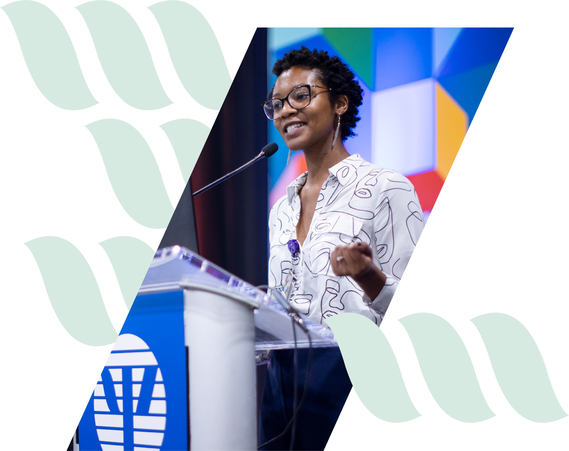 Speaker at podium, smiling on stage with colorful backdrop and microphone.