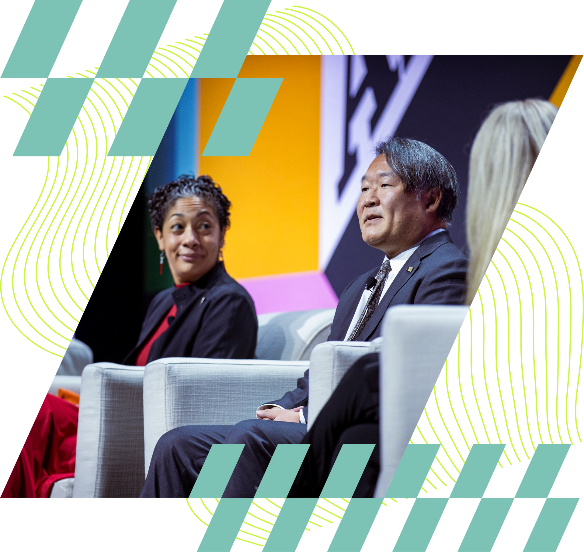 Two speakers seated on stage in armchairs, listening during a panel discussion.