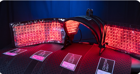 Red LED light therapy panels curved around a dark treatment table with hand and face cutouts
