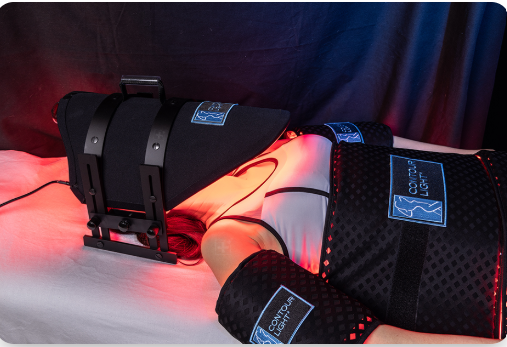 Black medical limb support braces on a person's arm and leg with blue labels, lit by red light