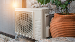 A white air conditioner is sitting on the side of a building next to a potted plant.