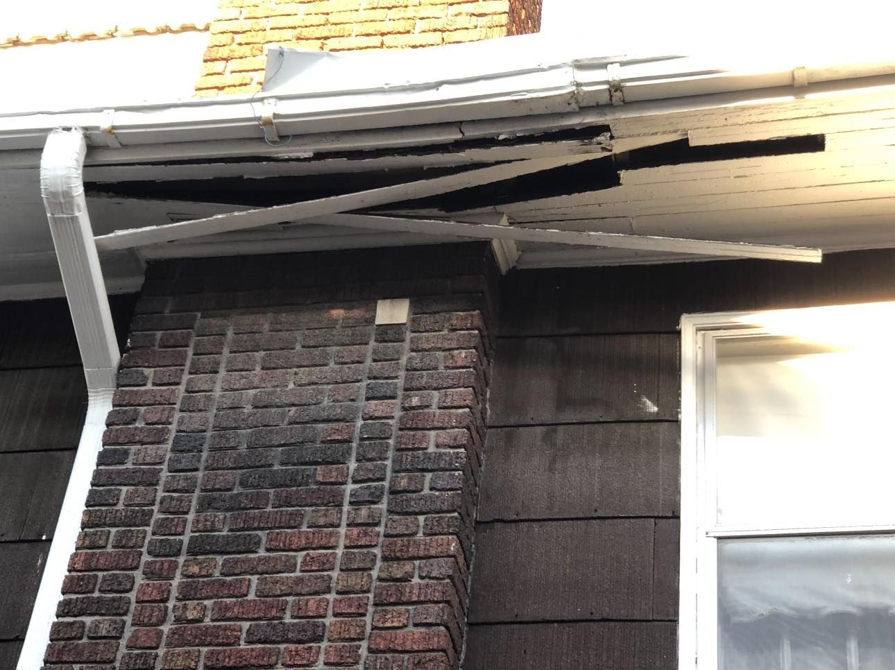 A brick building with a broken gutter and a window