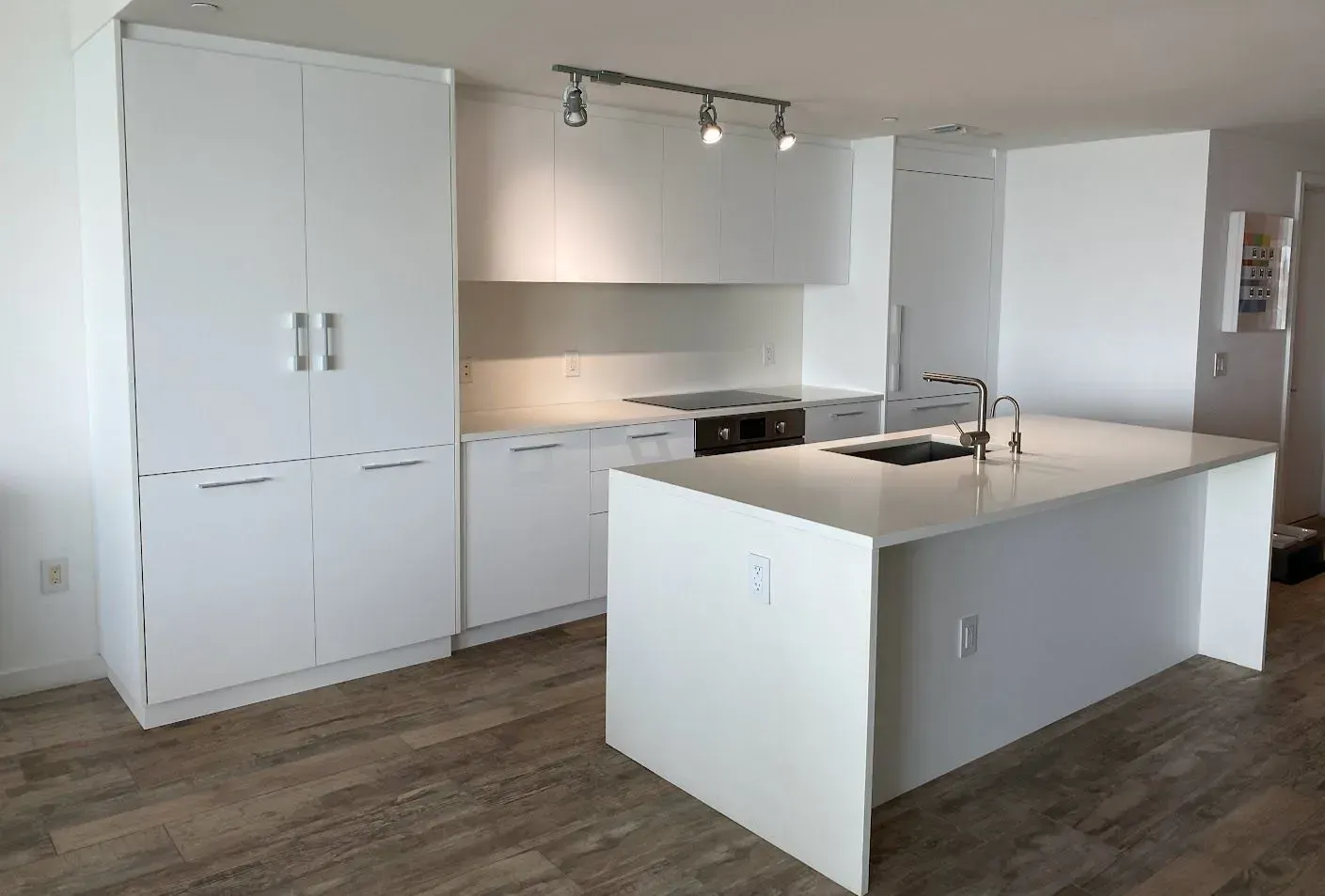 A kitchen with white cabinets and quartz countertop and dark wood floors.