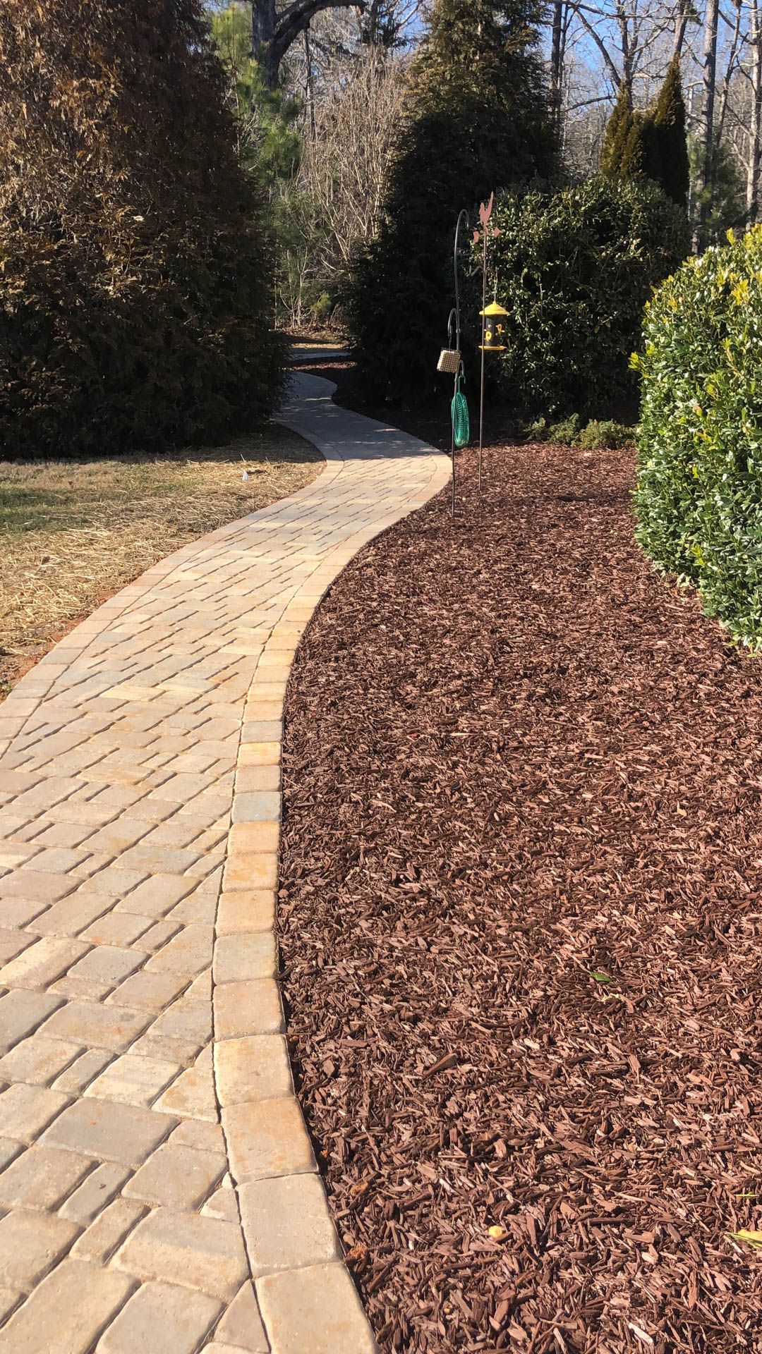 Brick pathway curves through a garden with brown mulch and green shrubbery.