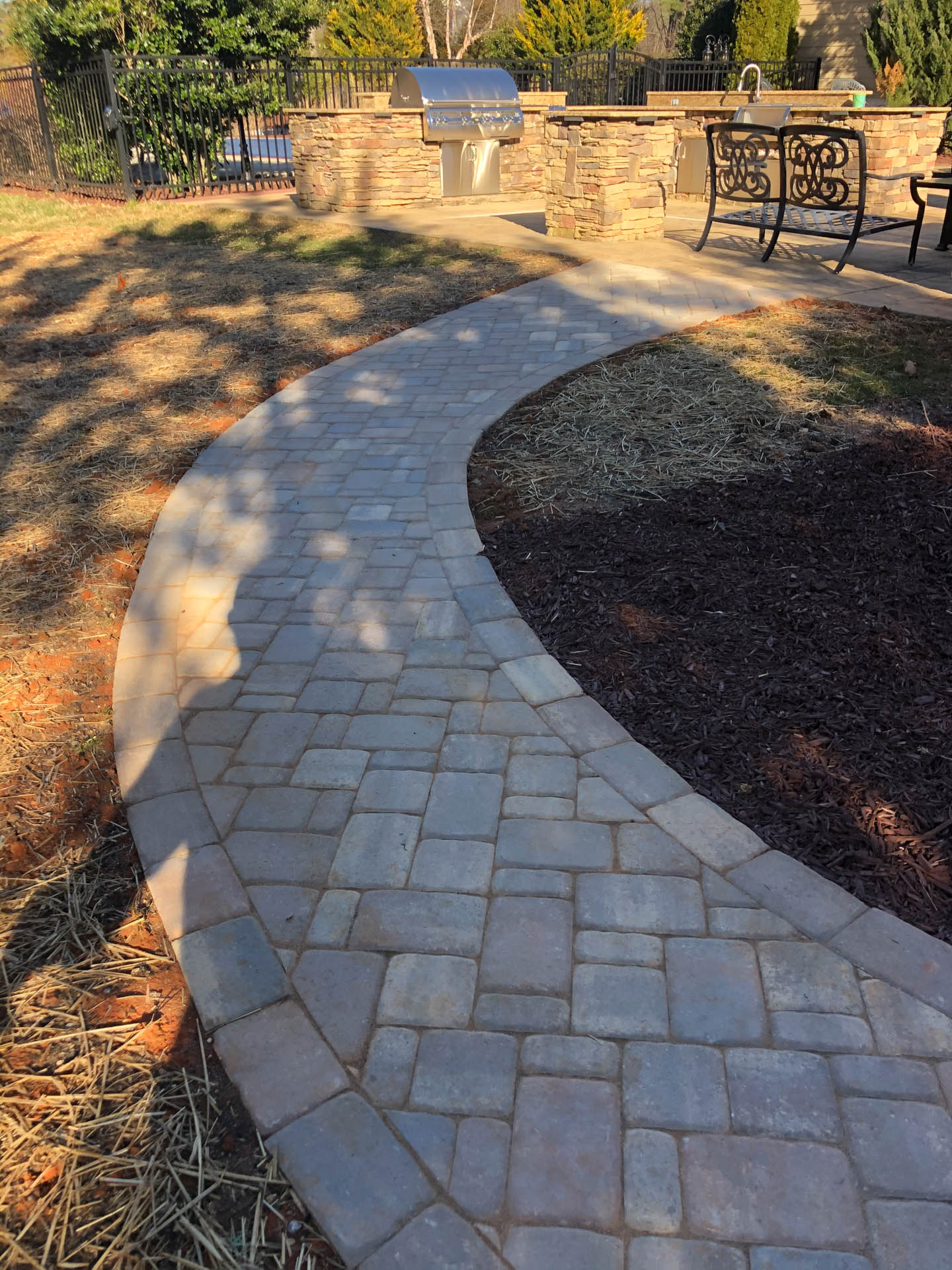 Curving paved walkway leading to an outdoor kitchen and patio.