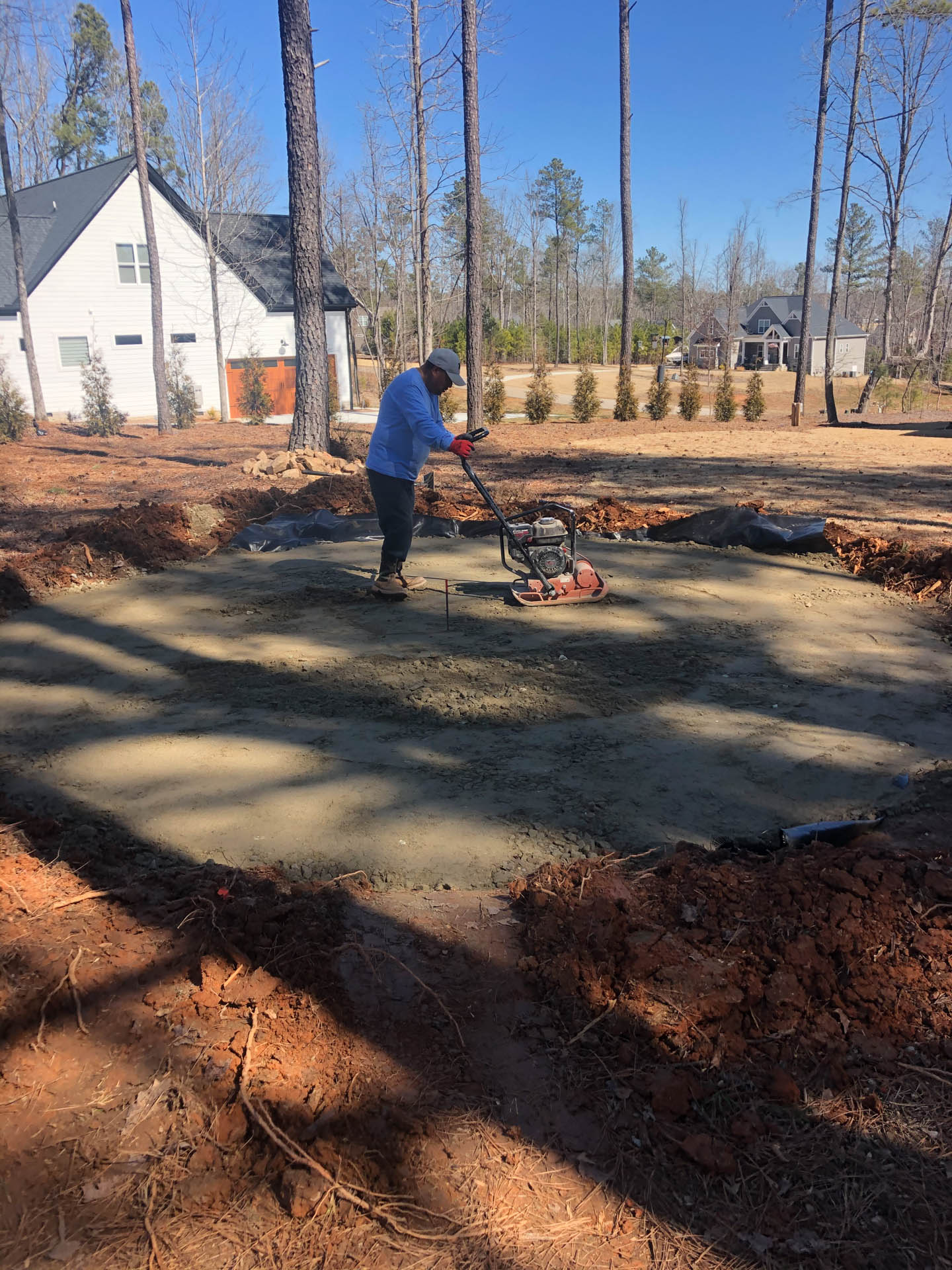 Man compacting gravel base for a patio or foundation with a vibrating plate compactor outdoors.