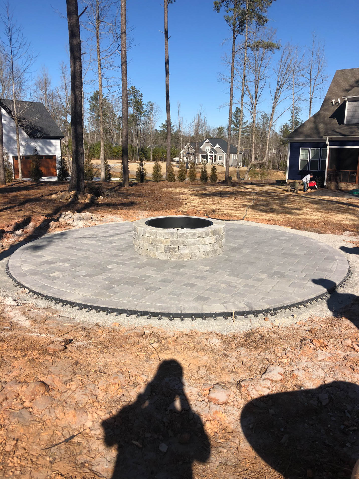 Circular stone patio with fire pit, under construction in a yard.