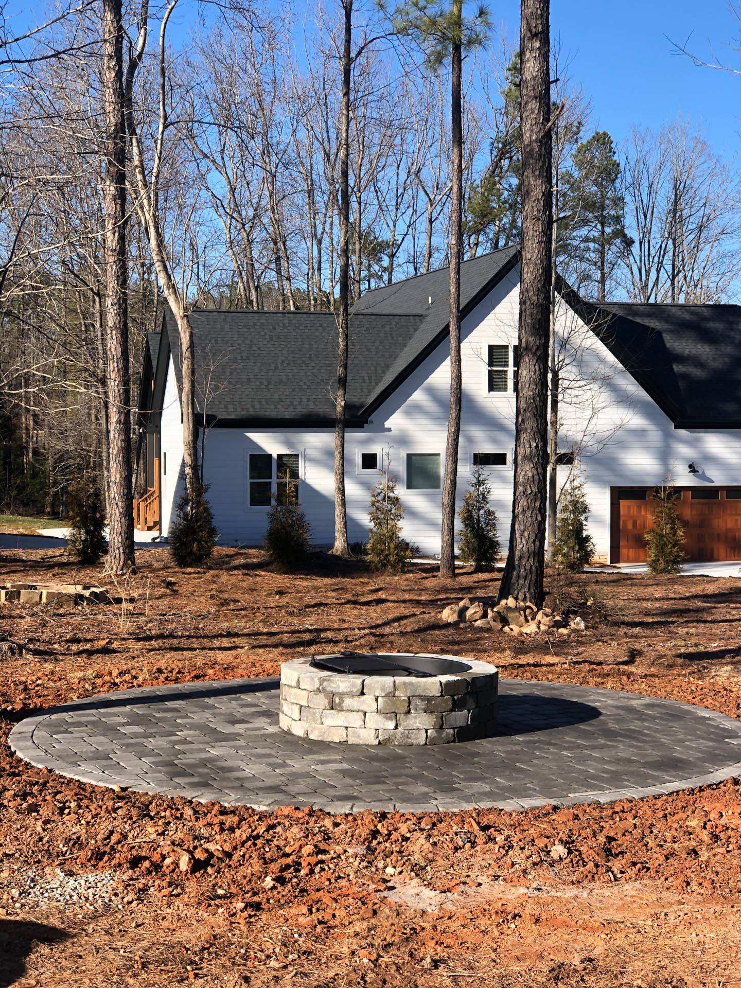 Fire pit on a brick patio in front of a white house with a dark roof.
