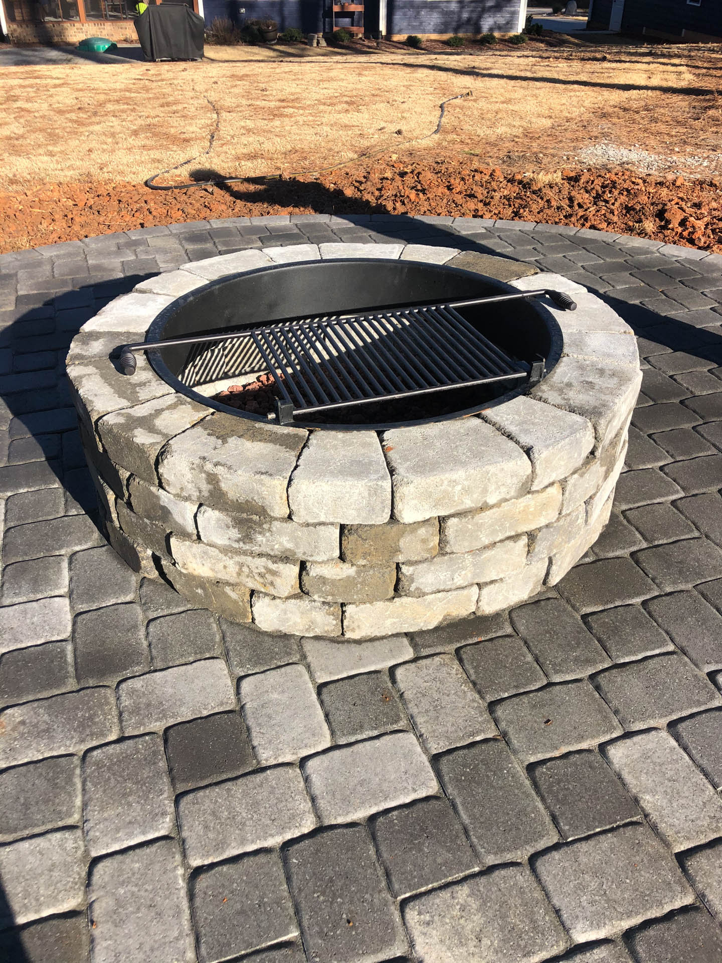 Stone fire pit with grill on a brick patio.
