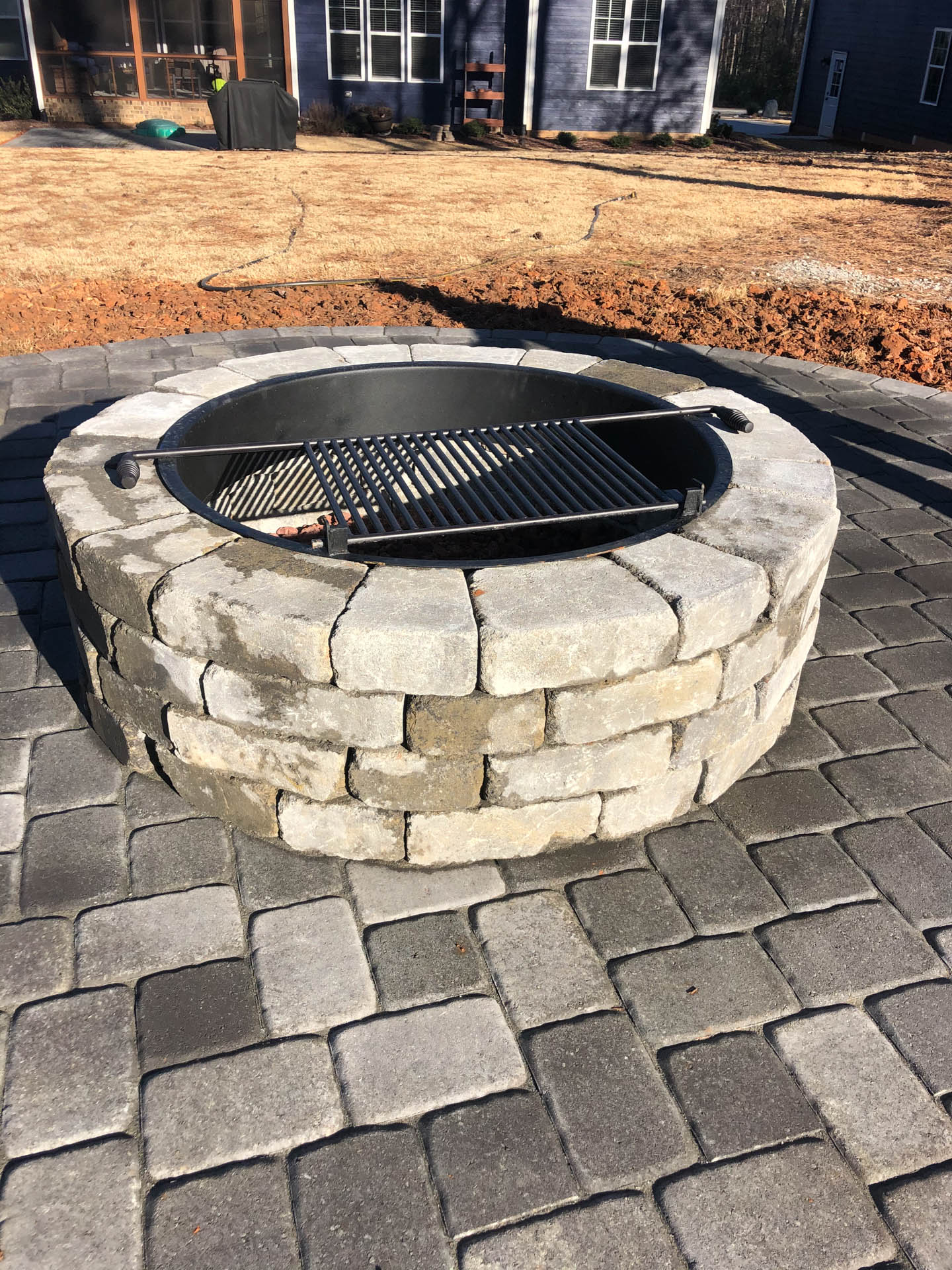 Stone fire pit with grill on a brick patio.