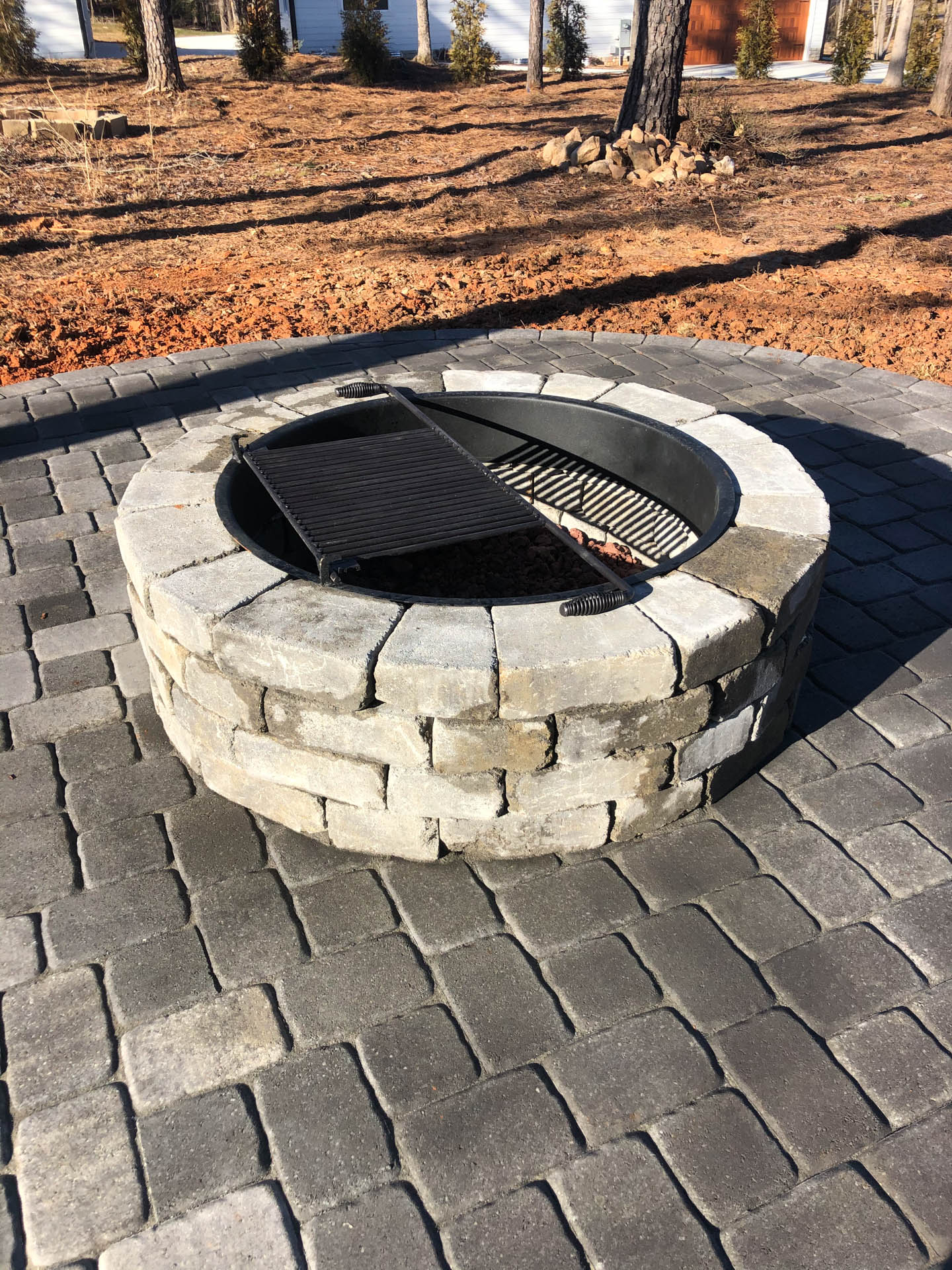 Round stone fire pit with metal grate on a brick patio.