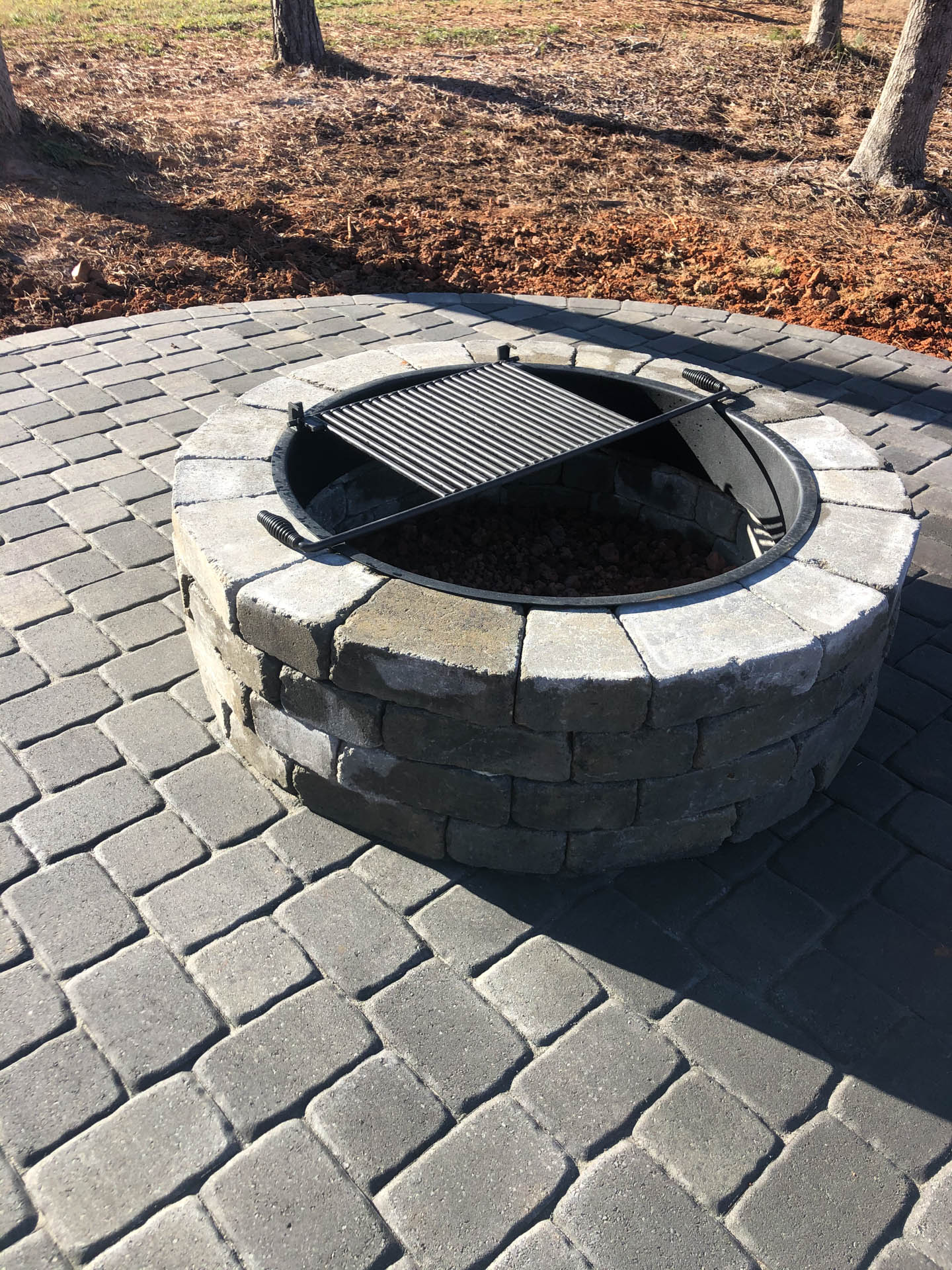 Brick fire pit with grill set on a brick patio in an outdoor setting.