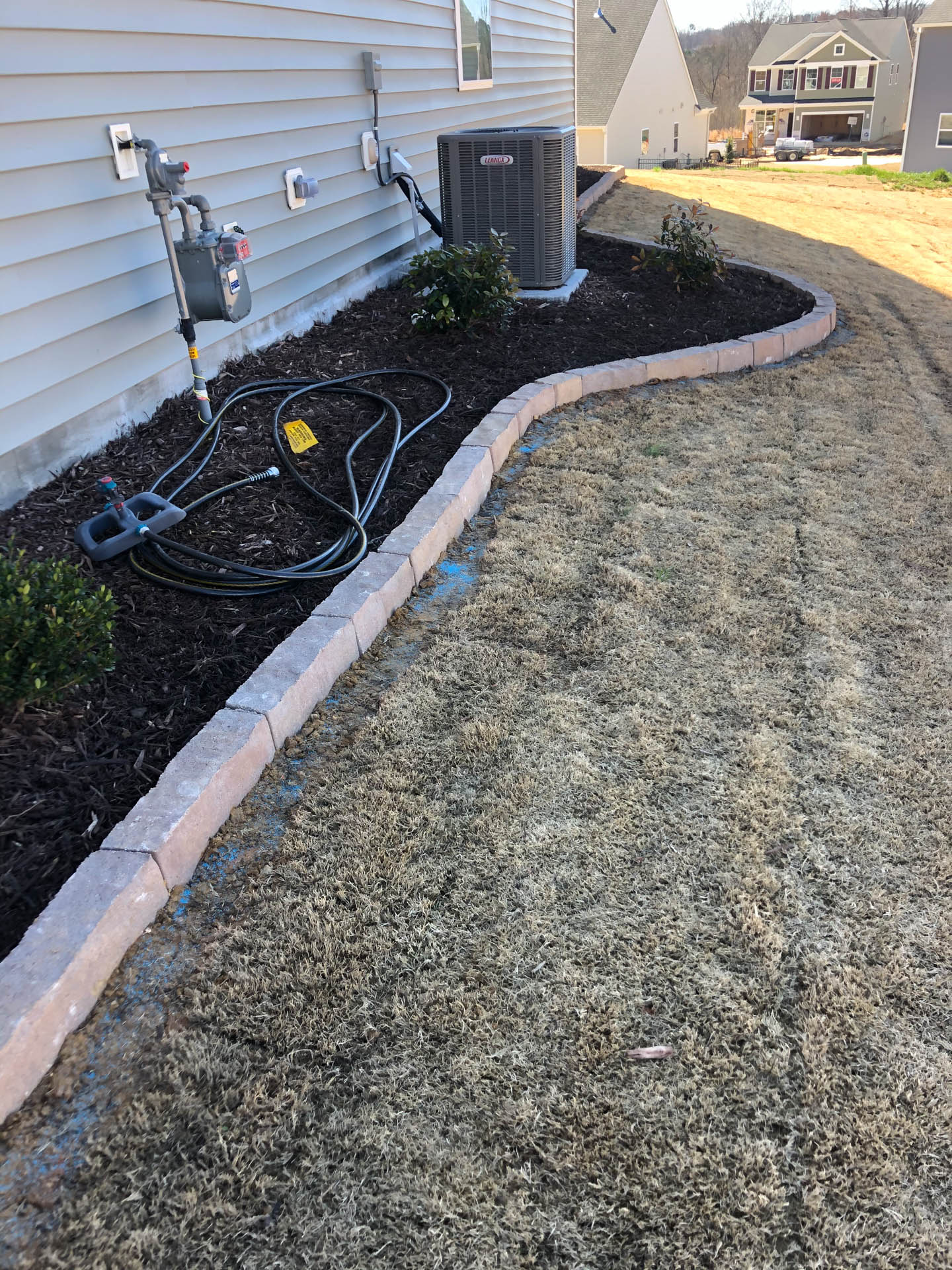 A low, brick-lined garden bed along a house with an air conditioner unit and gas meter.