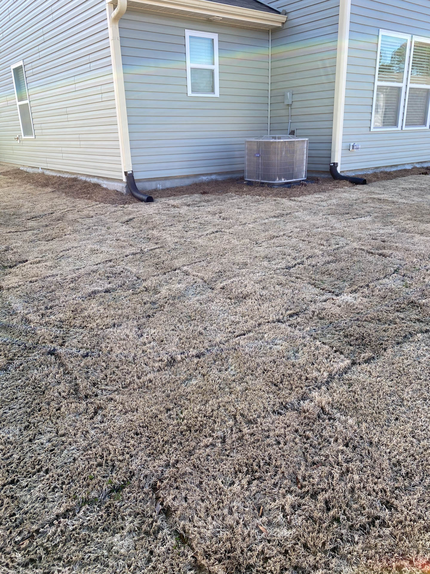 Dry brown grass and side of a house with air conditioning unit.