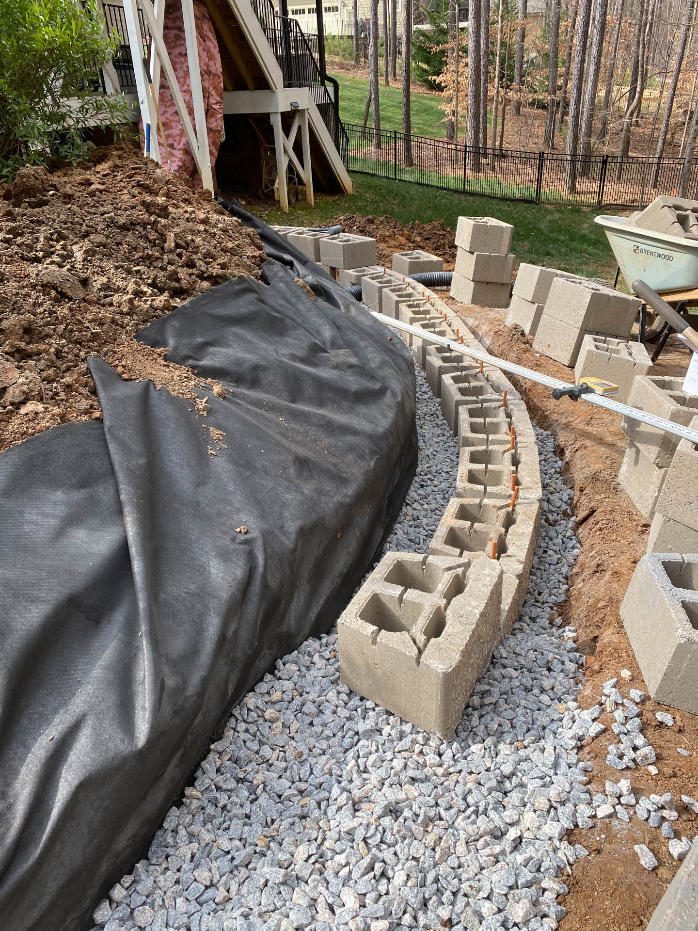 Construction of a curved retaining wall using concrete blocks, with gravel base and black landscape fabric.
