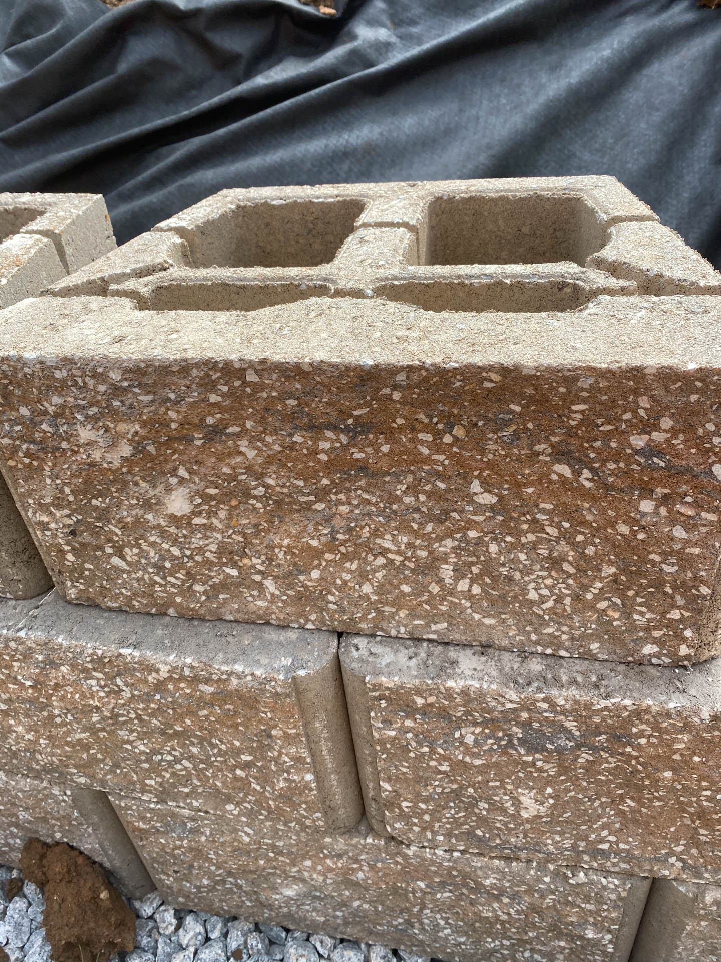 Stacked tan concrete blocks with holes, possibly for a retaining wall, resting on gravel.