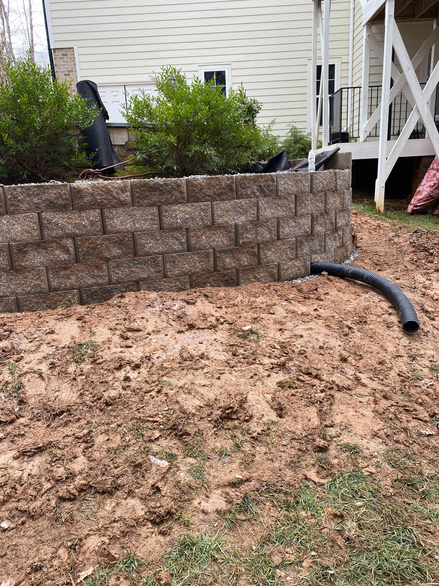 Brown retaining wall with a drainage pipe, surrounded by dirt and grass.