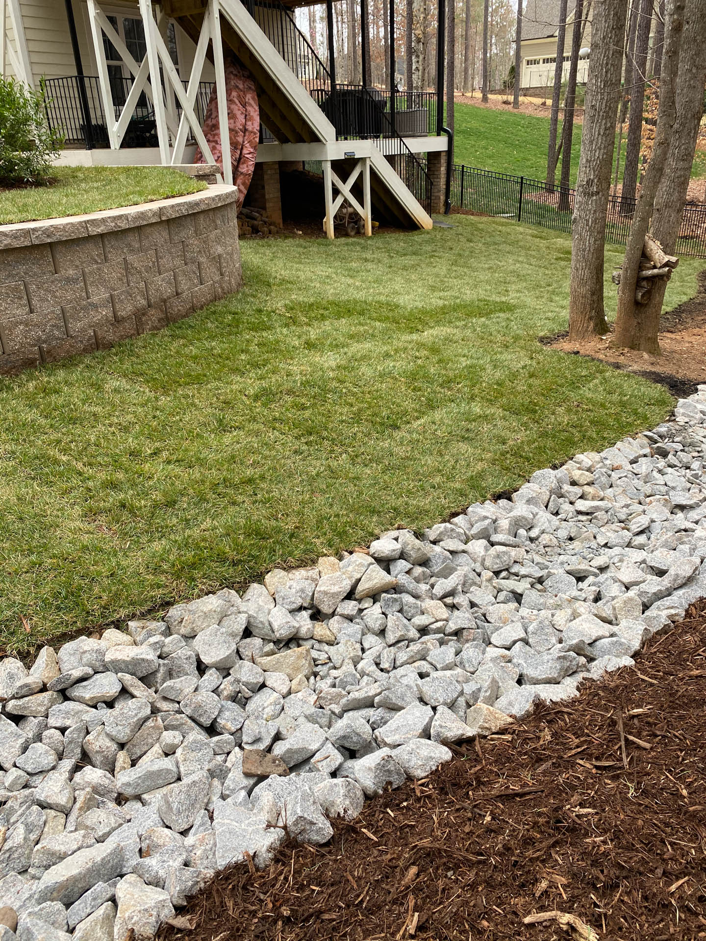 Grassy lawn with a stone-lined drainage channel next to a house with a deck.