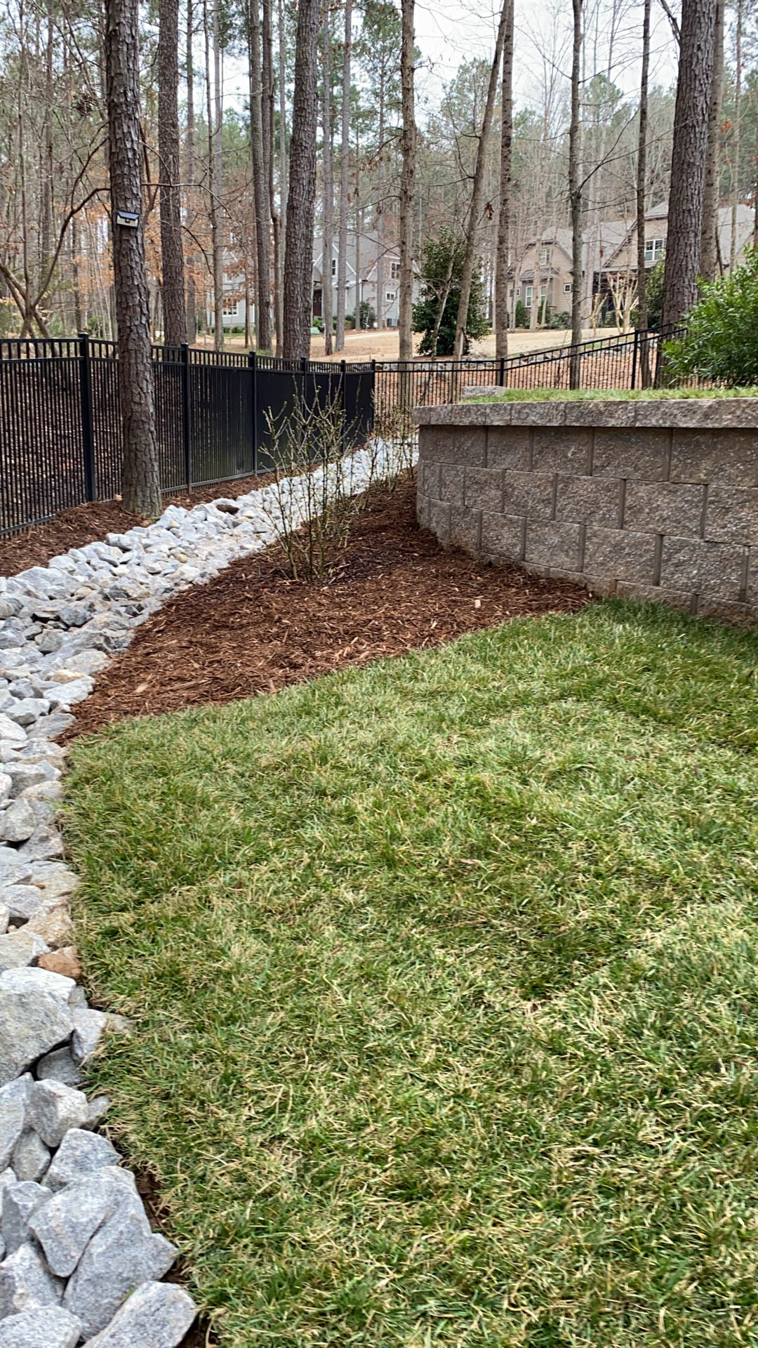 A landscaped yard with new grass, rock bed, mulch, and retaining wall.