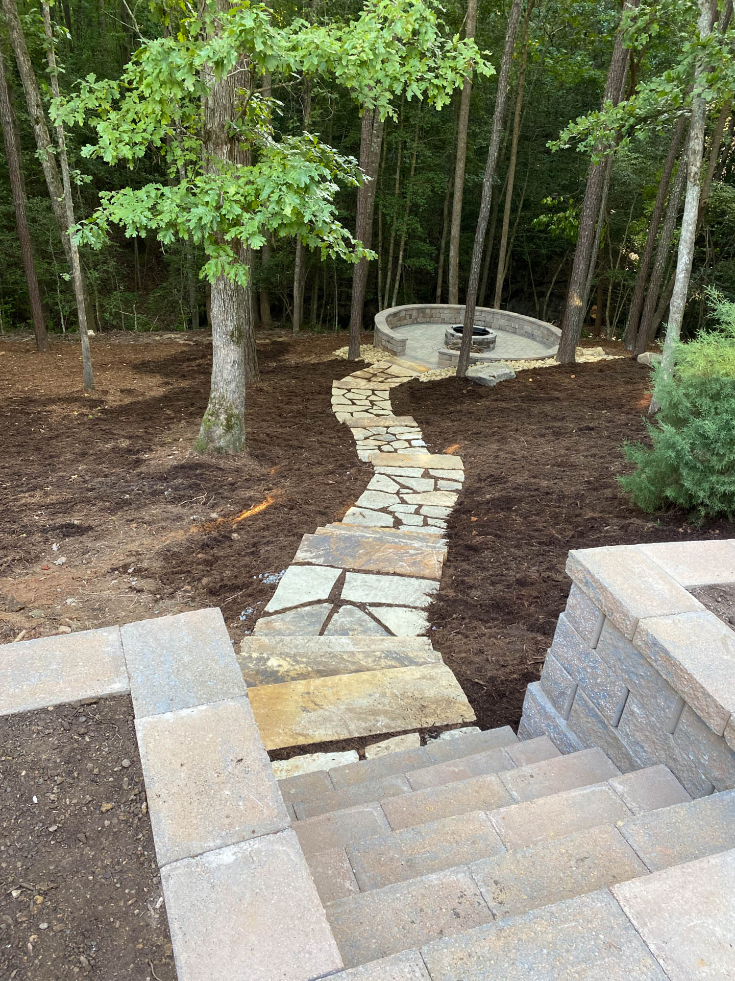 Stone path leading to a fire pit in a wooded yard; steps in the foreground.